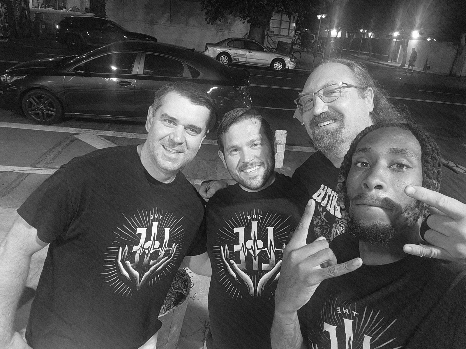 Four band members taking a group selfie outdoors at night